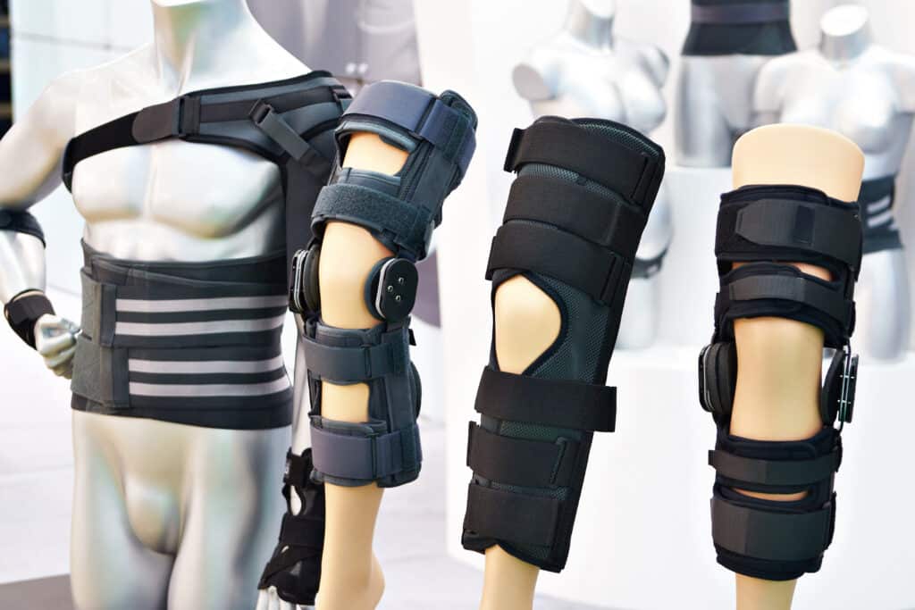 Présentation de supports orthopédiques noirs sur mannequins : attelle de dos, deux modèles d'orthèses de genou articulées et une chevillère.