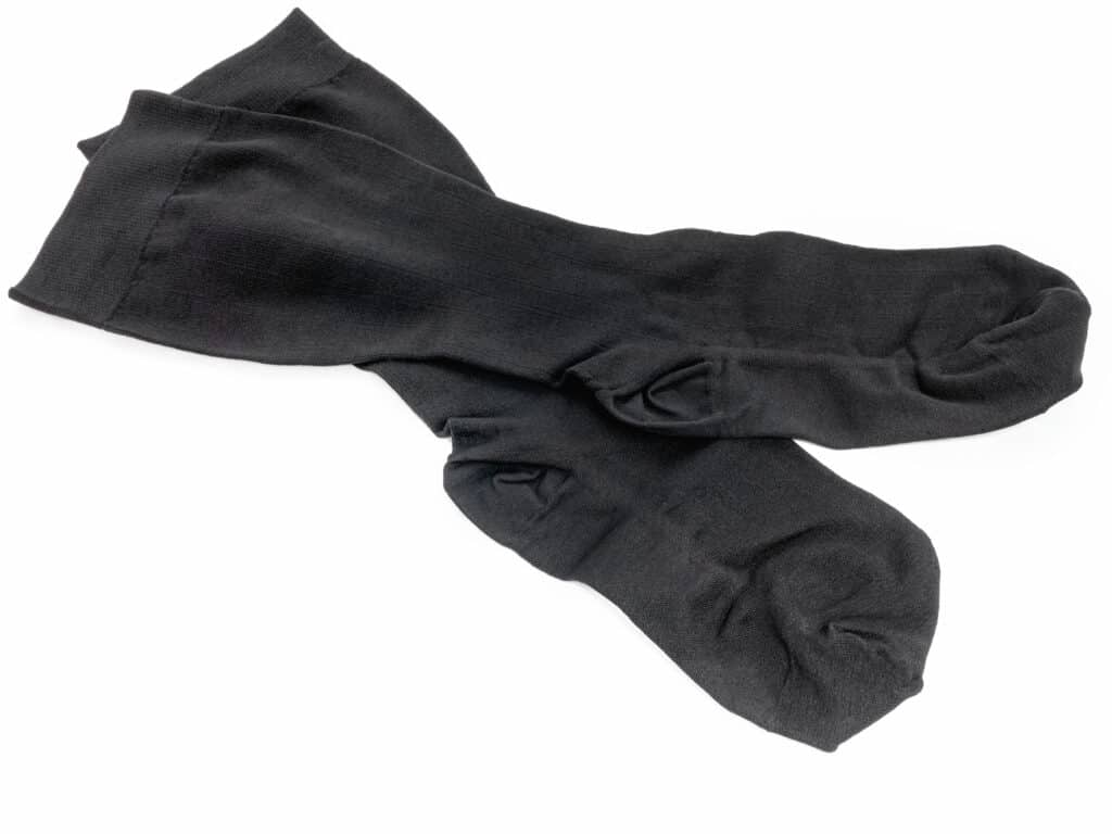 Deux chaussettes noires, opaques et côtelées, croisées sur un fond blanc uni, présentant des détails au niveau du talon.