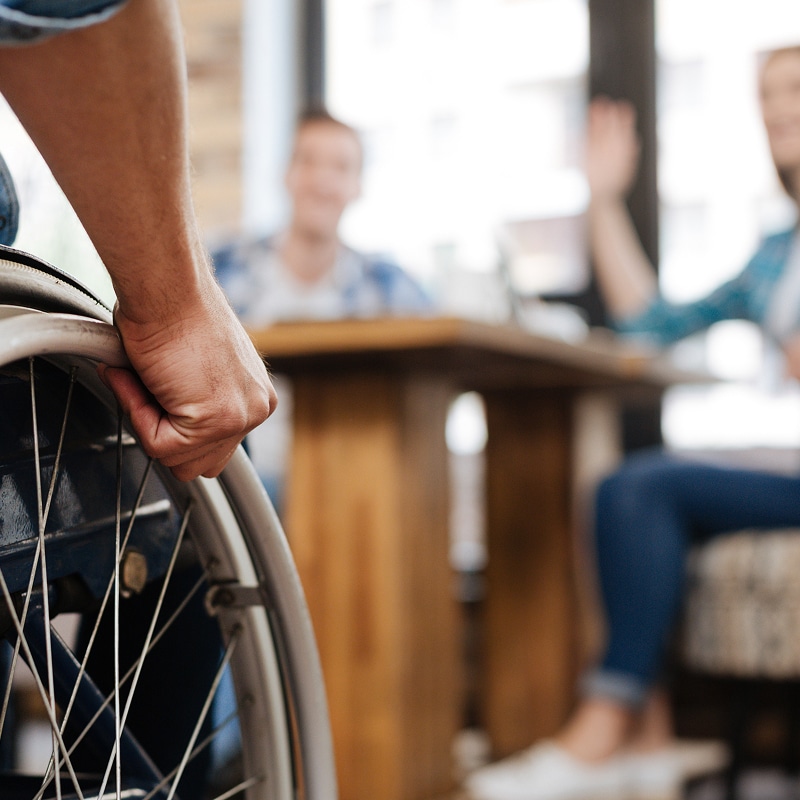 Gros plan sur la main d'une personne en fauteuil roulant saisissant la roue, saluant des amis assis à une table.