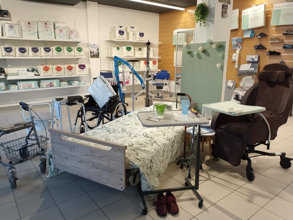 Magasin d'équipement médical montrant un lit, un fauteuil releveur, un déambulateur, un fauteuil roulant et des étagères de protections Pampers.